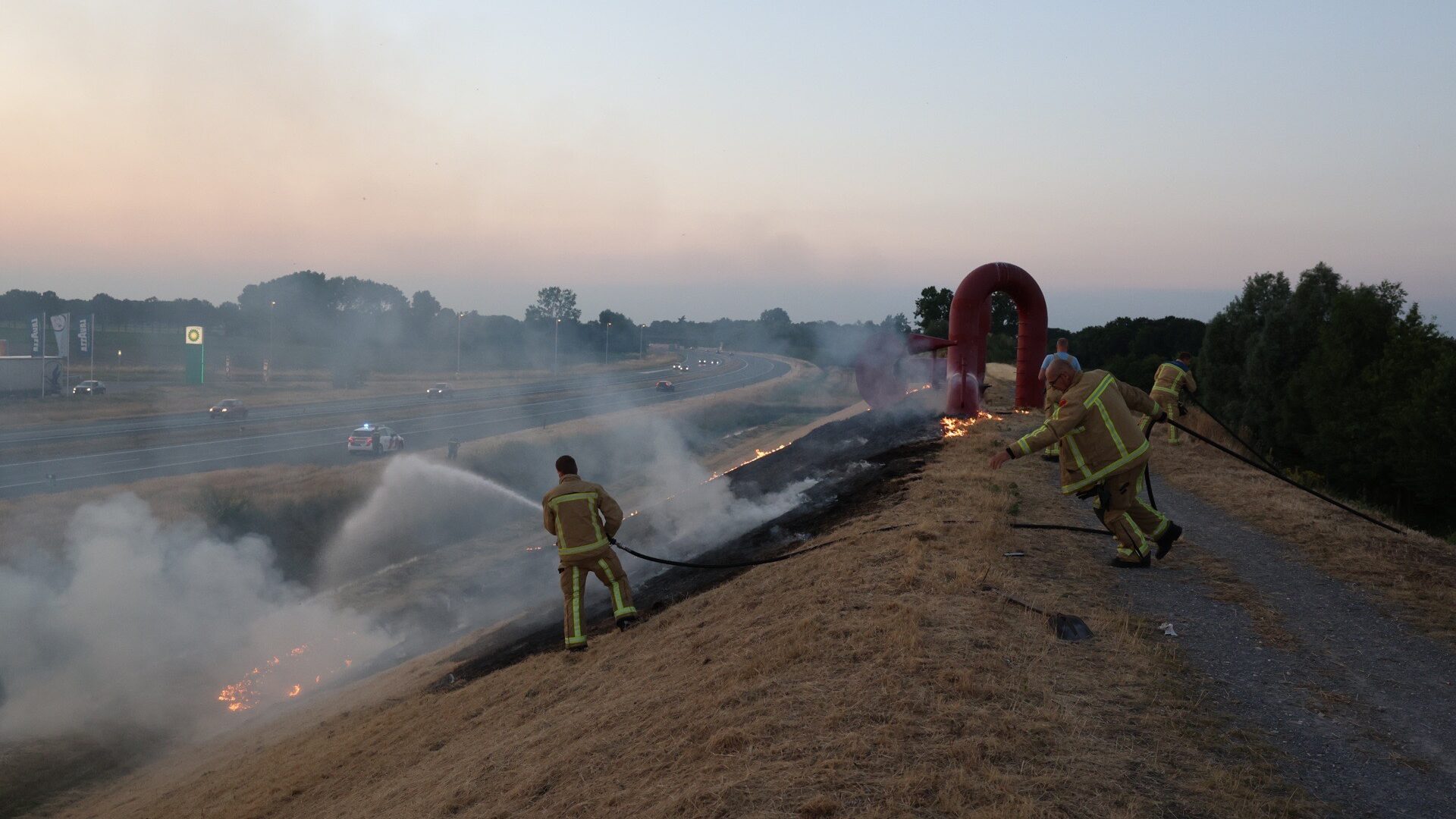 Brandweer blust de bermbrand op de geluidswal langs de A50