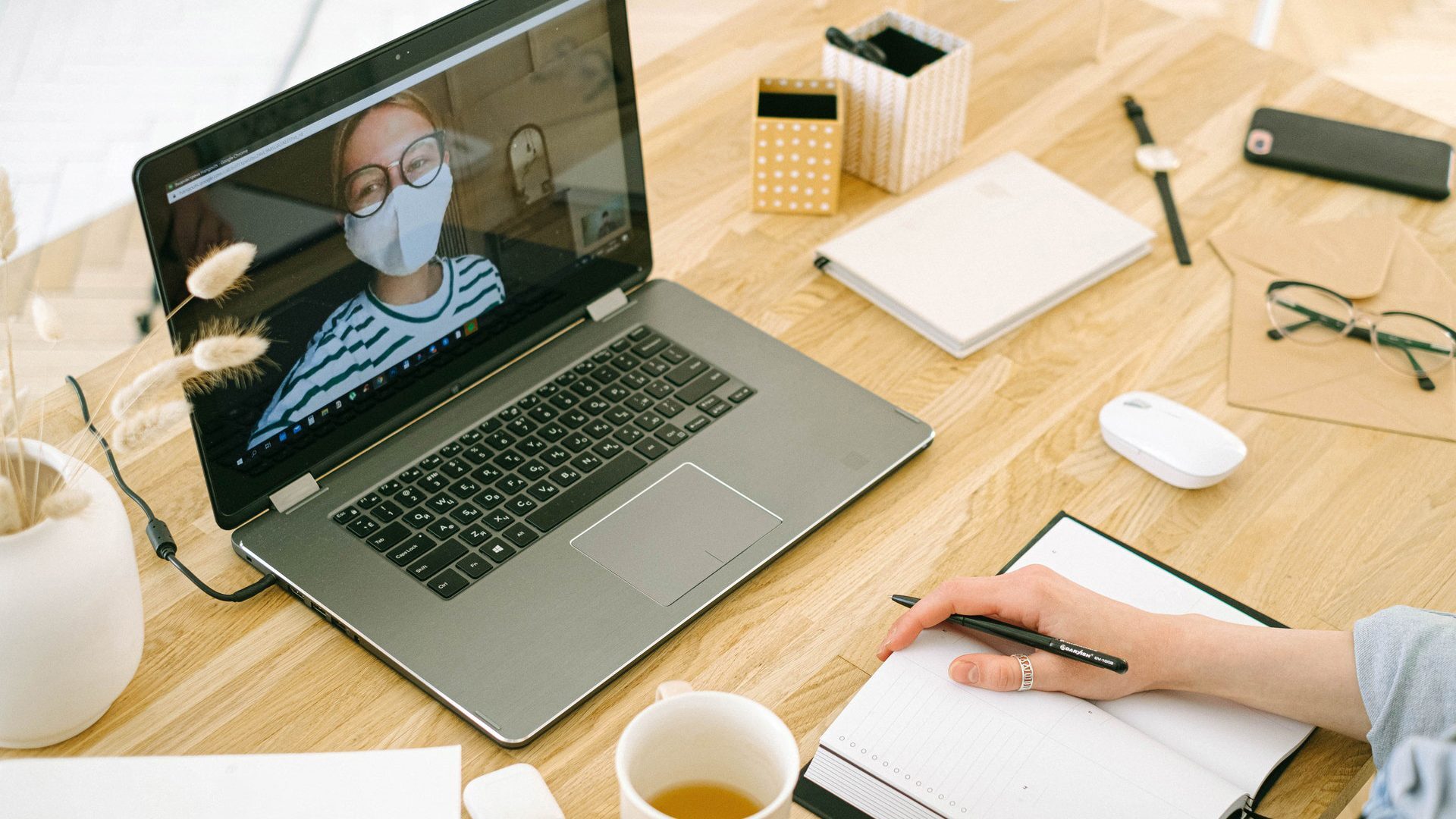 Videobellen op een laptop aan een bureau met iemand die een mondkapje op heeft