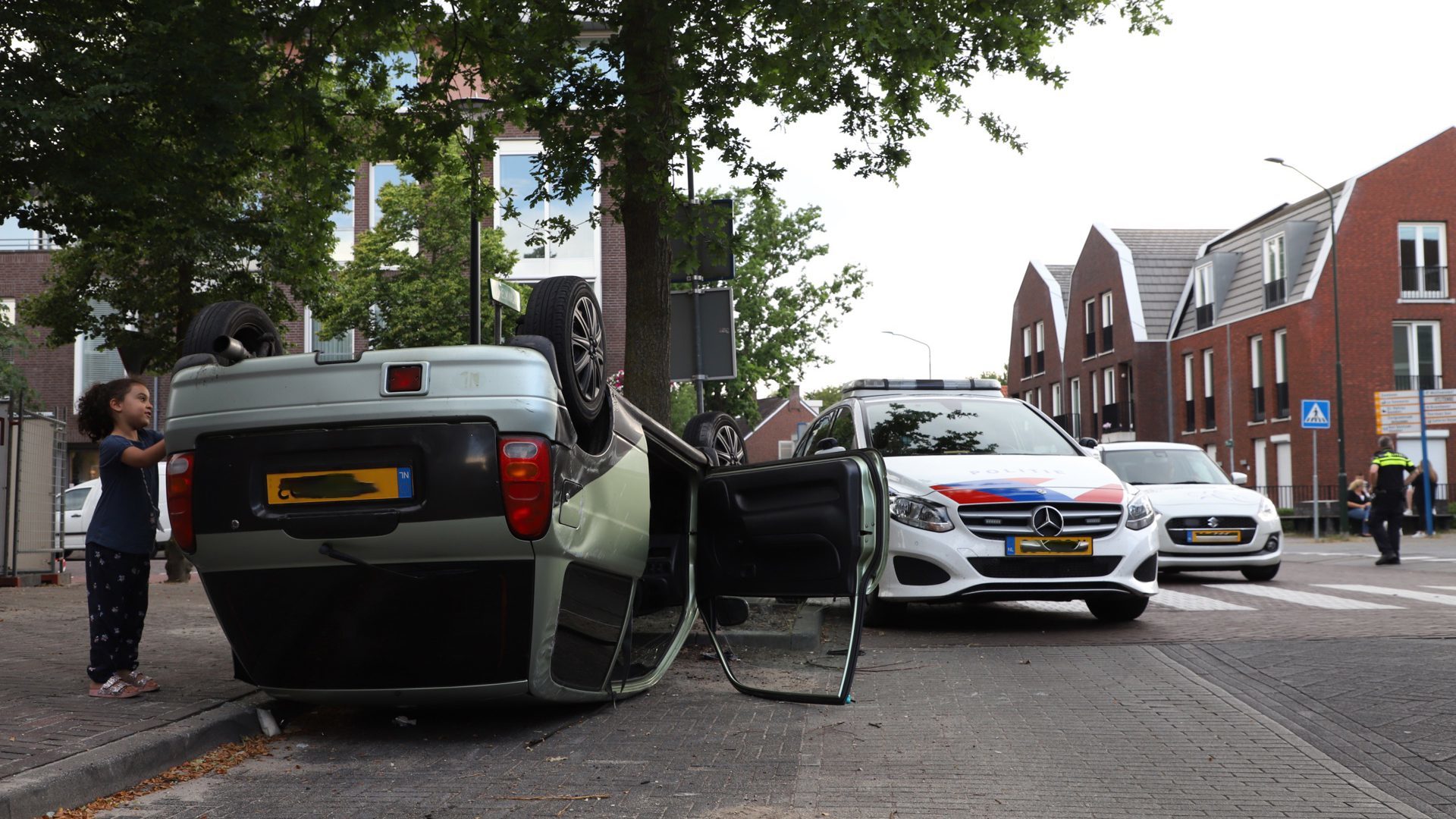 Een groene auto op z'n kop in een parkeervak met twee politieautos